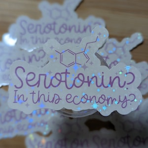 May include: A white sticker with a purple design that says "Serotonin? In this economy?" with a chemical structure of serotonin in the background. The sticker has a holographic finish with blue glitter.