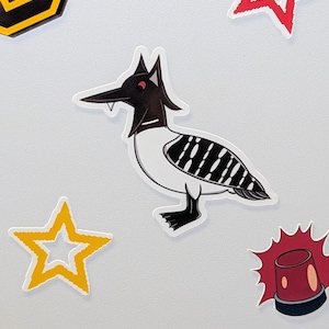 Puede incluir: Una pegatina de un pájaro de dibujos animados con cabeza y pico negros, cuerpo blanco y espalda a rayas negras. Alrededor del pájaro hay pegatinas de estrellas y sirenas en rojo, amarillo y negro.