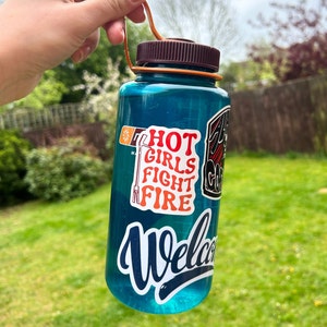 May include: A blue reusable water bottle with a brown lid and a carrying handle. The bottle has several stickers on it, including one that says "Hot Girls Fight Fire".