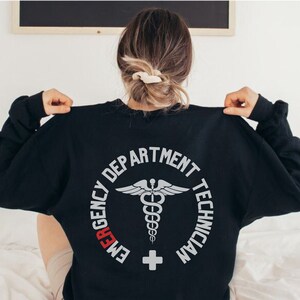 May include: Black sweatshirt with a white graphic of a medical symbol and the text "Emergency Department Technician".