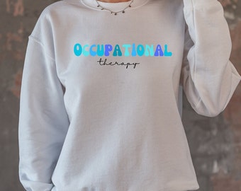 Puede incluir: Sudadera blanca con el texto "OCCUPATIONAL therapy" en letras azules y azul claro.