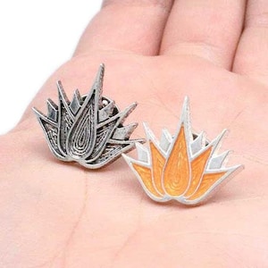 May include: Two silver-toned metal pins with a stylized flower design. One pin is silver, and the other is orange.