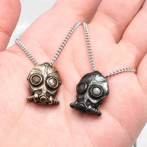 May include: Two silver chain necklaces with gas mask pendants. One pendant is silver and the other is gold.