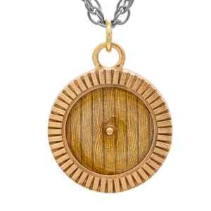 May include: A gold pendant necklace with a round wooden door charm. The door is made of wood with a grain pattern and has a small knob in the center. The pendant is surrounded by a decorative gold frame.