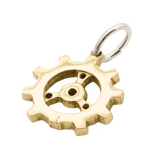Könnte beinhalten: Ein goldfarbener Metall-Zahnrad-Anhänger mit einem silbernen Sprungring. Das Zahnrad hat ein detailliertes Design mit einer zentralen Nabe und Speichen.