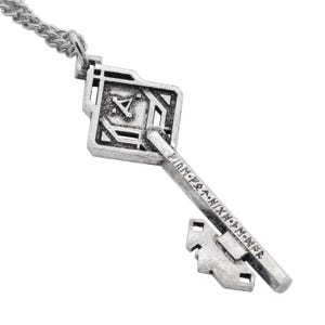 May include: A silver key necklace with a square-shaped key head and a detailed design. The key head features a symbol and the key shaft is inscribed with runes.