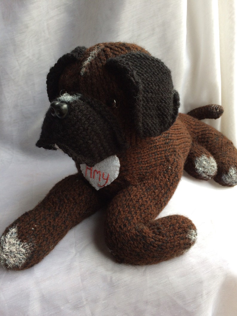 May include: A brown and black knitted dog toy with white accents. The toy has a heart-shaped tag with the name "Amy" embroidered on it.
