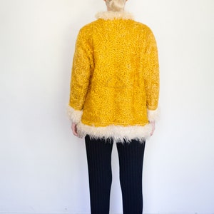 Puede incluir: Una chaqueta amarilla y peluda con ribete de piel blanca. La chaqueta la lleva puesta una persona con el pelo rubio, pero la persona no es visible en la imagen.
