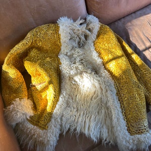 Puede incluir: Una chaqueta de terciopelo amarillo con intrincados bordados florales. La chaqueta est&aacute; forrada con piel sint&eacute;tica blanca.