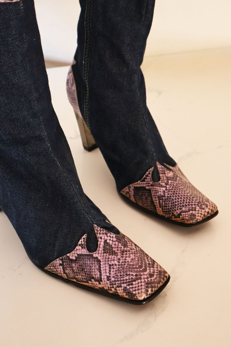 Może przedstawiać: Para niebieskich dżinsowych but&oacute;w z wężowym wzorem na palcach i pięcie. Buty mają szpiczasty nos i gruby obcas.