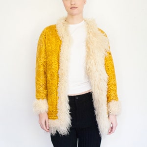 Puede incluir: Una chaqueta de ante amarilla con cuello y ribetes de piel sint&eacute;tica blanca. La chaqueta tiene un dise&ntilde;o bordado floral.
