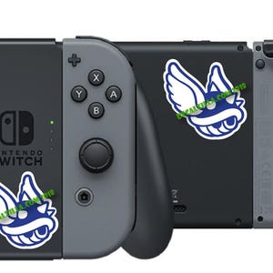 May include: A gray Nintendo Switch console with a blue and white Koopa Troopa sticker on the left side and a blue and white Koopa Troopa sticker on the right side. The console is in a closed position.