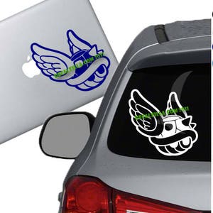 May include: A white car with a blue and white sticker of a winged turtle shell on the back window. The sticker has the text "decalvilla.com/toy11" on it.