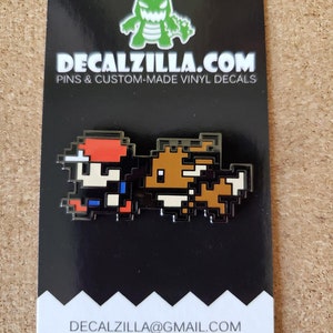May include: A black and white enamel pin featuring a pixelated image of a video game character, Mario, and a brown and white pixelated image of a dog. The pin is on a black background with white text that reads "DECALZILLA.COM PINS & CUSTOM-MADE VINYL DECALS" and "DECALZILLA@GMAIL.COM @decalzilla".