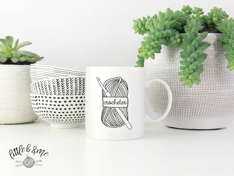May include: White ceramic mug with a black and white illustration of a ball of yarn and crochet hook. The text "crocheter" is written on the mug.
