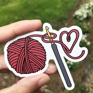 May include: A red yarn ball with a crochet hook and yarn forming a heart shape.
