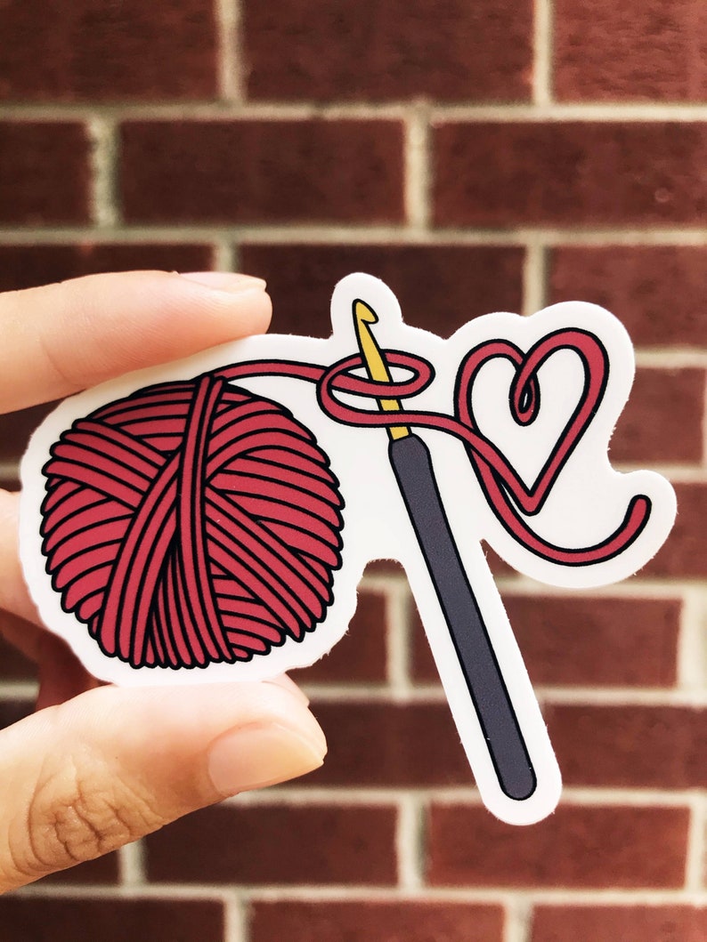 May include: A red yarn ball, a crochet hook, and a red yarn heart shape.