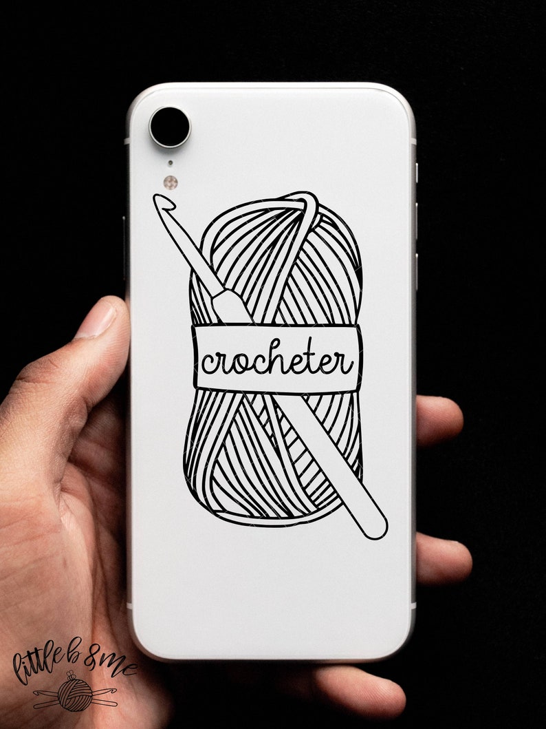 May include: White phone case with a black and white illustration of a ball of yarn and a crochet hook. The yarn ball has a label that says "crocheter".