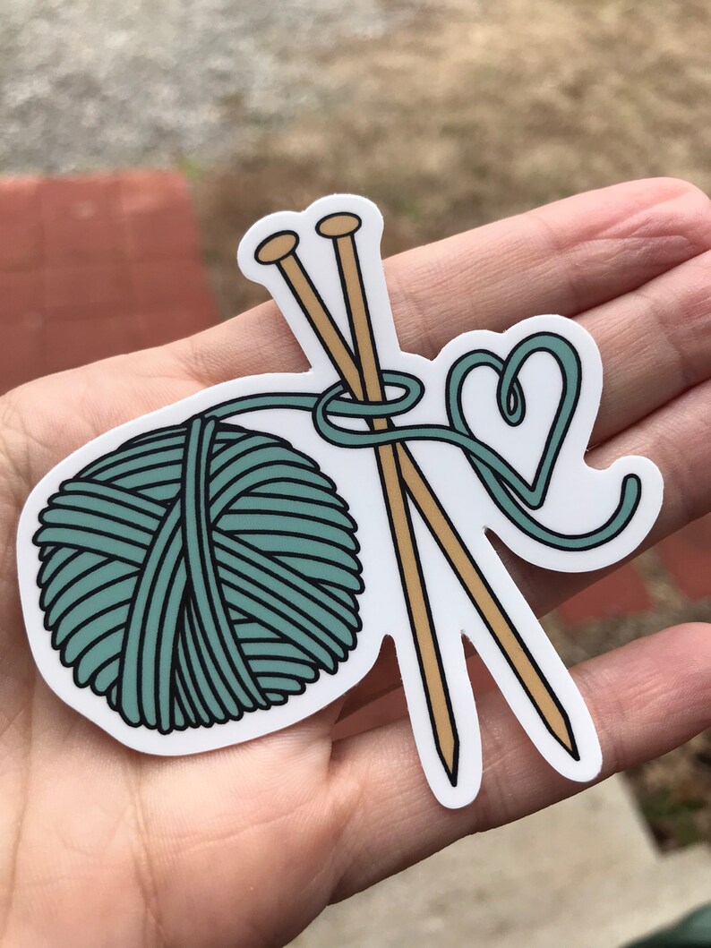 May include: A teal yarn ball with two wooden knitting needles and a teal yarn heart.