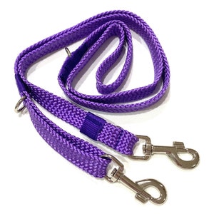 May include: A purple dog lead with a braided design. The lead has two sections with silver metal clasps and a loop handle. The lead is made of a durable, woven material.