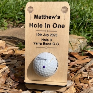 May include: A wooden golf ball display with the text "Matthew's Hole In One" and the date "19th July 2023". A golf ball is held in place. The display also includes the text "Hole 3 Yarra Bend G.C."