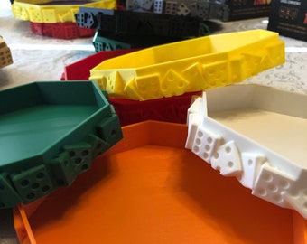 Puede incluir: Un conjunto de seis bandejas de dados octogonales en varios colores, incluyendo verde, naranja, blanco, amarillo, rojo y negro. Cada bandeja tiene un diseño único de dados alrededor del borde.