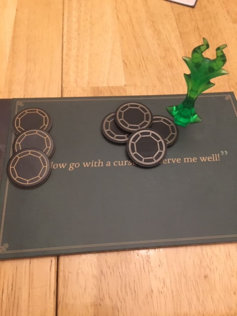 Puede incluir: Una figura en miniatura de pl&aacute;stico verde de una criatura con cuernos y una cola larga, de pie sobre una superficie de fieltro verde. Hay seis fichas negras y doradas en la superficie. El texto "Now go with a curse to serve me well!" est&aacute; impreso en la superficie.