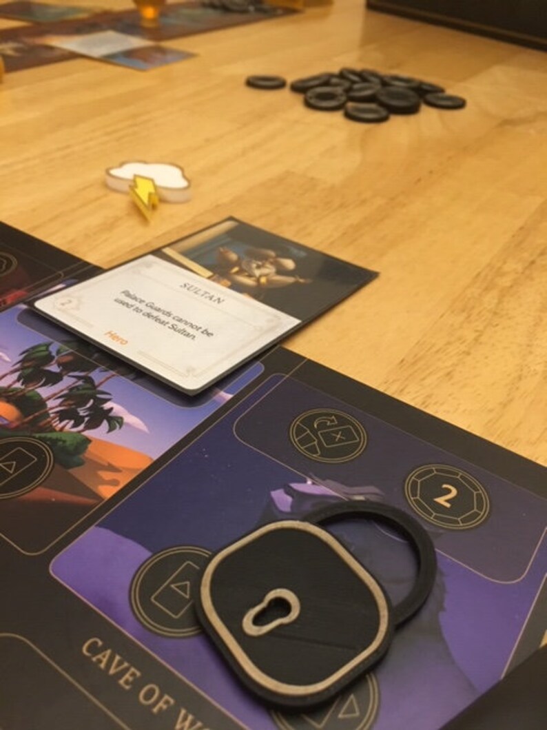 Puede incluir: Un token de cerradura negro con un ojo de cerradura dorado y un borde dorado. El token est&aacute; en un juego de mesa con un fondo morado y el texto "CAVE OF W" en letras doradas. El texto "SULTAN" es visible en una tarjeta en el fondo.