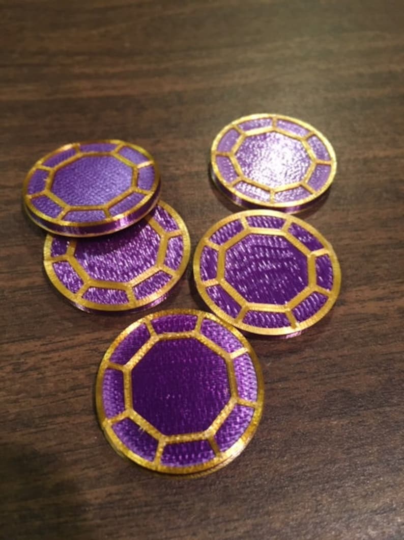 Puede incluir: Cinco fichas octogonales de color p&uacute;rpura y dorado con una superficie texturizada.