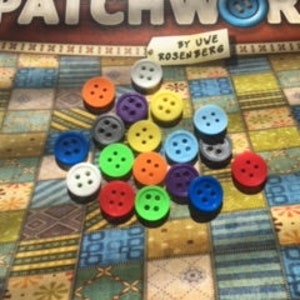 May include: A collection of colorful plastic buttons in various shades of blue, green, red, orange, yellow, and gray. The buttons are arranged in a random pattern on a patterned surface.
