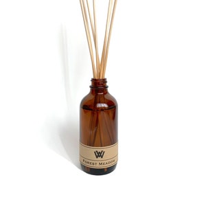 Puede incluir: Un difusor de aroma en botella de vidrio marrón con palitos de madera y una etiqueta que dice "W FOREST MEADOW".