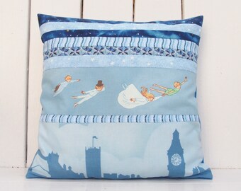 May include: A blue and white pillow with a Peter Pan theme. The pillow features a scene of Peter Pan, Wendy, and the Lost Boys flying through the air. The background is a blue sky with stars. The pillow is made of a soft, comfortable fabric.