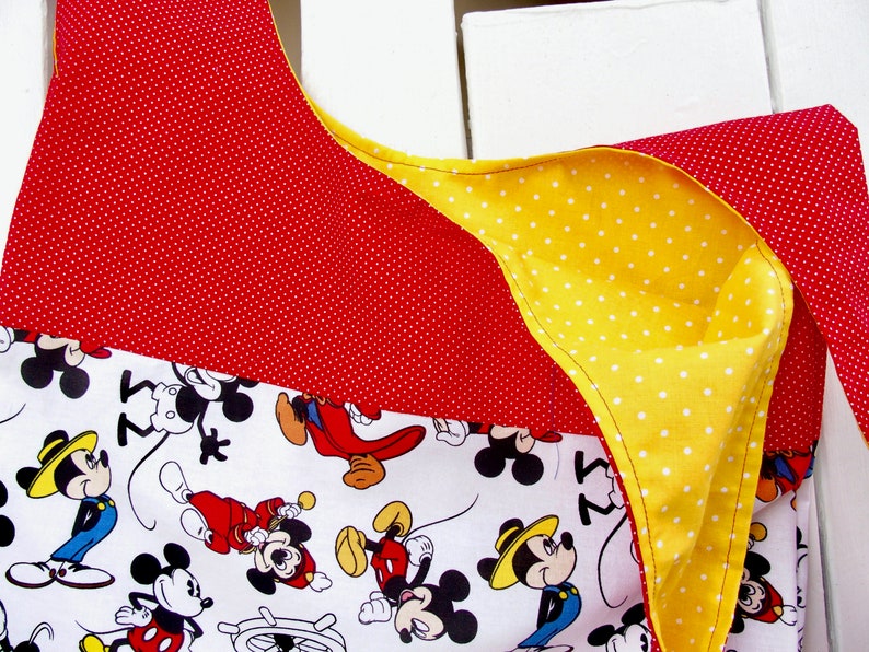 May include: A red and yellow fabric tote bag with a white background featuring a repeating pattern of Mickey Mouse characters. The bag has a polka dot pattern on the red and yellow fabric.