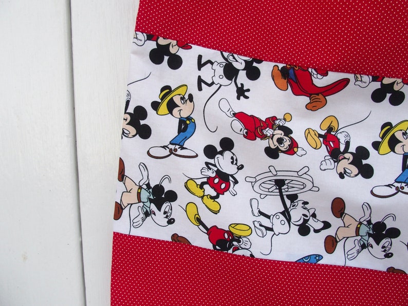 May include: White fabric with a red polka dot pattern. The fabric has a white panel with a repeating pattern of Mickey Mouse characters in various poses. The characters are in black, red, yellow, and blue.