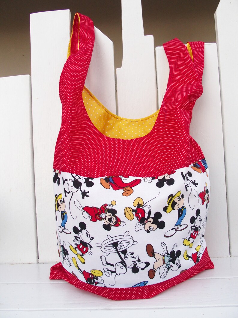 May include: Red and yellow fabric tote bag with white polka dots. The bag features a white fabric panel with a repeating pattern of Mickey Mouse characters.