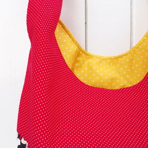 May include: A red and yellow fabric tote bag with white polka dots. The bag has a wide, rounded opening and a yellow fabric lining with white polka dots.
