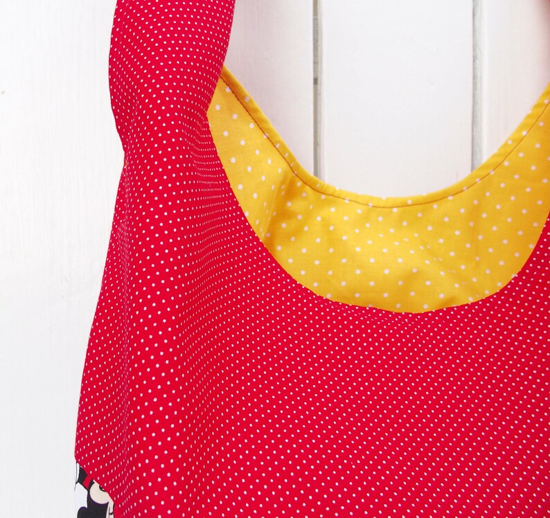 May include: A red and yellow fabric tote bag with white polka dots. The bag has a wide, rounded opening and a yellow fabric lining with white polka dots.