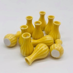 Peut inclure: Un groupe de 10 petits vases en céramique jaune avec un motif côtelé. Les vases sont disposés en pile sur une surface blanche.