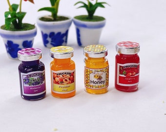 Può includere: Quattro vasetti di vetro in miniatura con coperchi argentati ed etichette colorate. I vasetti contengono diversi tipi di marmellata e miele. Le etichette riportano "Smucker's", "Marmellata di mirtilli", "Marmellata di pesca", "Miele" e "Marmellata di fragole".