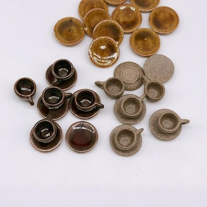 Peut inclure: Plusieurs petits services à thé miniatures en céramique marron et beige. Les ensembles comprennent de petites tasses, soucoupes et assiettes. Les services à thé sont disposés sur une surface blanche.