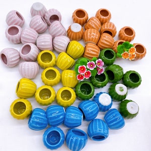 May include: A collection of colorful miniature ceramic pots in various shapes and sizes. The pots are arranged in a circular pattern on a white surface. Some of the pots are decorated with flowers.