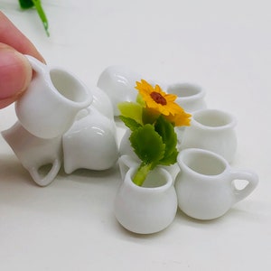 May include: A set of miniature white ceramic pots with a single yellow sunflower in one of the pots. The pots are perfect for dollhouses or miniature gardens.