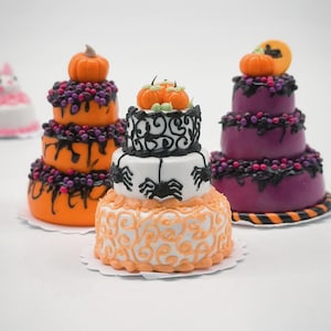 Puede incluir: Mini pasteles de Halloween en naranja, blanco y morado. Cada pastel es de varios niveles y está decorado con calabazas, arañas y bayas de color púrpura oscuro. Los pasteles se colocan sobre blondas de papel blanco, perfectos para la decoración de Halloween.