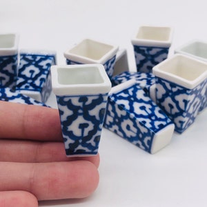 May include: Set of ten small, white ceramic planters with a blue and white floral pattern. The planters are square shaped with a slightly tapered base.