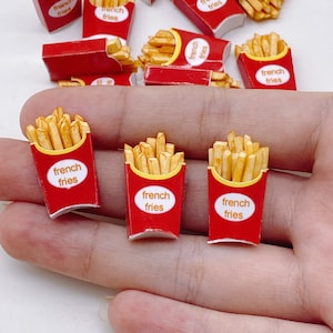 May include: Miniature red and yellow French fry containers with the words "french fries" printed on them. The containers are filled with golden-brown fries. Several containers are scattered across the surface.