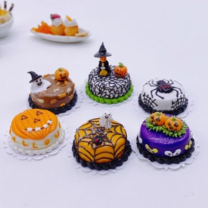 Pode incluir: Seis bolos em miniatura com tema de Halloween decorados com abóboras, fantasmas, aranhas e desenhos de teias de aranha. Os bolos estão em guardanapos de papel brancos.