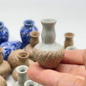 May include: A collection of small ceramic vases in various shades of blue and brown. The vases are all different shapes and sizes, and some have a textured finish.