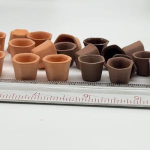 May include: A selection of small, terracotta-coloured miniature flower pots. Some pots are a lighter shade of brown, while others are a darker, richer brown. A ruler is in the foreground, providing scale.
