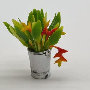 Könnte beinhalten: Ein Strauß orangefarbener, gelber und roter Blumen mit grünen Blättern in einem silbernen Metalleimer.