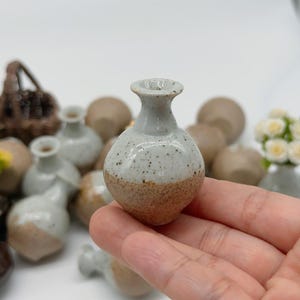 May include: A small, handcrafted ceramic vase with a speckled white upper half and a brown lower half. The vase has a rounded body and a narrow neck. Other similar vases are in the background.